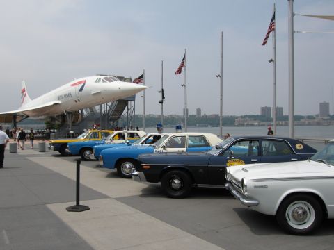 1991 Ford LTD Crown Victoria - British Airways Concorde displayed beside a row of classic American police cars on a waterfront pier with the river and flags in view.