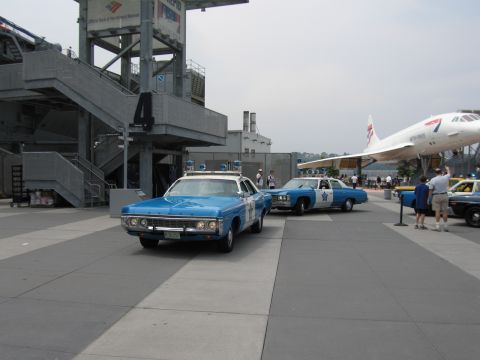 1991 Ford LTD Crown Victoria - Two vintage blue-and-white police cars with star door emblems parked on a plaza beside a museum structure, with a Concorde visible in the b…