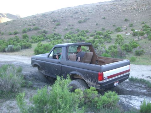 1987 Ford Bronco - A Ford Bronco navigates a muddy trail with two people inside.
