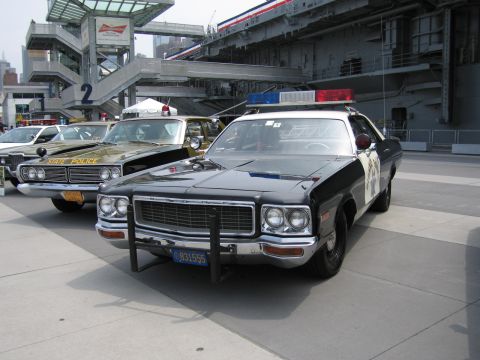 1991 Ford LTD Crown Victoria - black-and-white Highway Patrol sedan with a chrome push bar and roof lights parked beside other vintage police cars under a carrier structu…