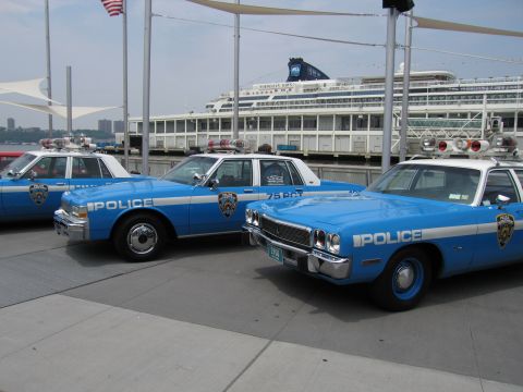 1991 Ford LTD Crown Victoria - Three vintage blue-and-white NYPD Police sedans with roof lights parked on a waterfront pier in front of a moored cruise ship.