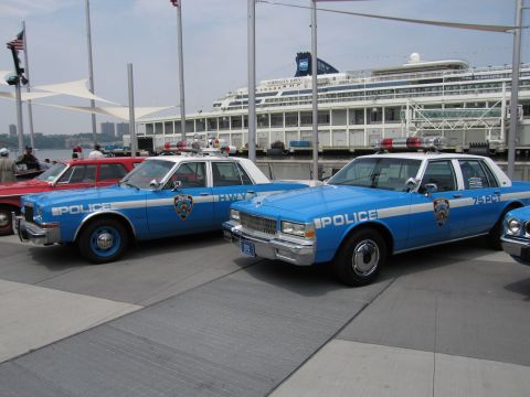 1991 Ford LTD Crown Victoria - Vintage blue-and-white NYPD Police sedans, one marked 75 PCT, parked side by side on a waterfront pier with a cruise ship behind.