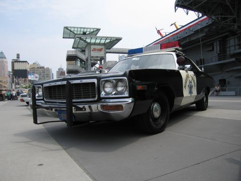 1991 Ford LTD Crown Victoria - black and white Dodge police cruiser with a brush guard, roof light bar, and gold star emblem parked on a waterfront plaza.