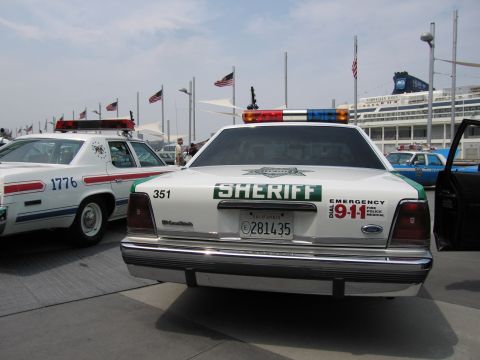 1991 Ford LTD Crown Victoria - White and green Ford Crown Victoria Sheriff cruiser marked EMERGENCY 911 and unit 351, displayed among police cars at a waterfront show.