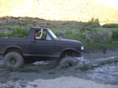 1987 Ford Bronco - Driver waves from a 1987 Ford Bronco as it navigates through a muddy off-road trail.
