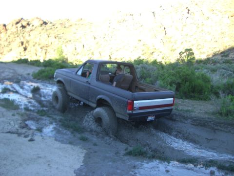 1987 Ford Bronco - This 1987 Ford Bronco navigates a challenging muddy path in a rural, hilly area.