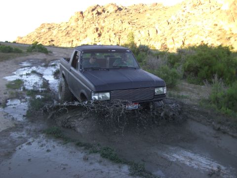 1987 Ford Bronco - This 1987 Ford Bronco is navigating a challenging muddy terrain, kicking up a large spray.