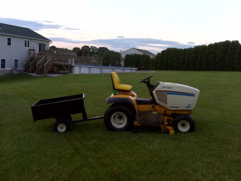 1994 Ford Bronco - A yellow and white Cub Cadet riding mower is parked on a grassy lawn, attached to a black utility trailer.
