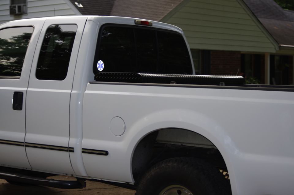 White pickup truck side view, showing a toolbox in the bed and an emblem on the rear window