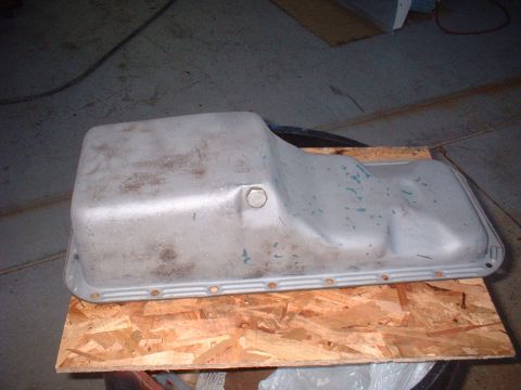 1968 Ford Mustang - A metal oil pan sits on a wooden surface, showing its bolt holes and a single bolt on top.