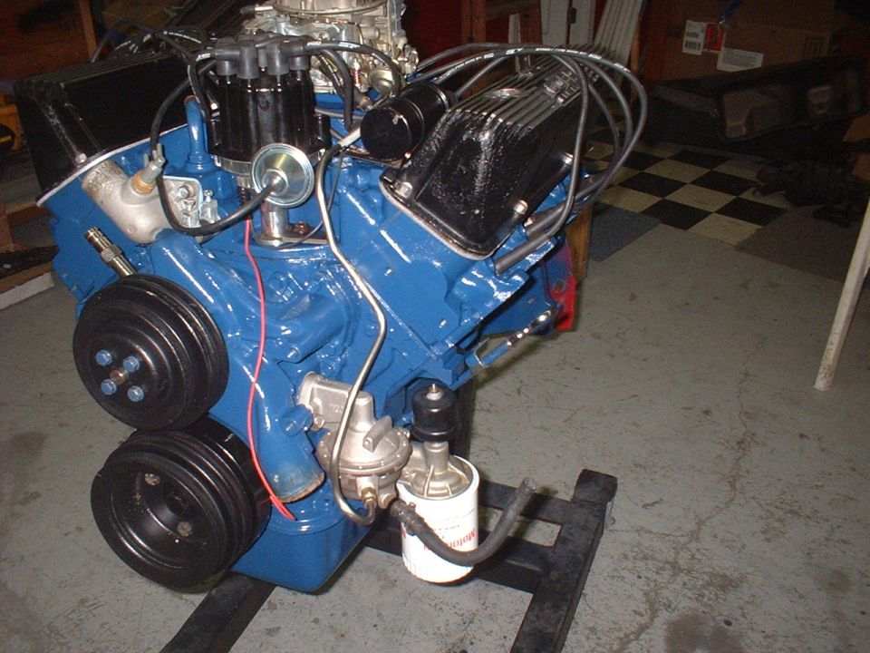 Blue V8 engine with black valve covers and chrome carburetor on a stand