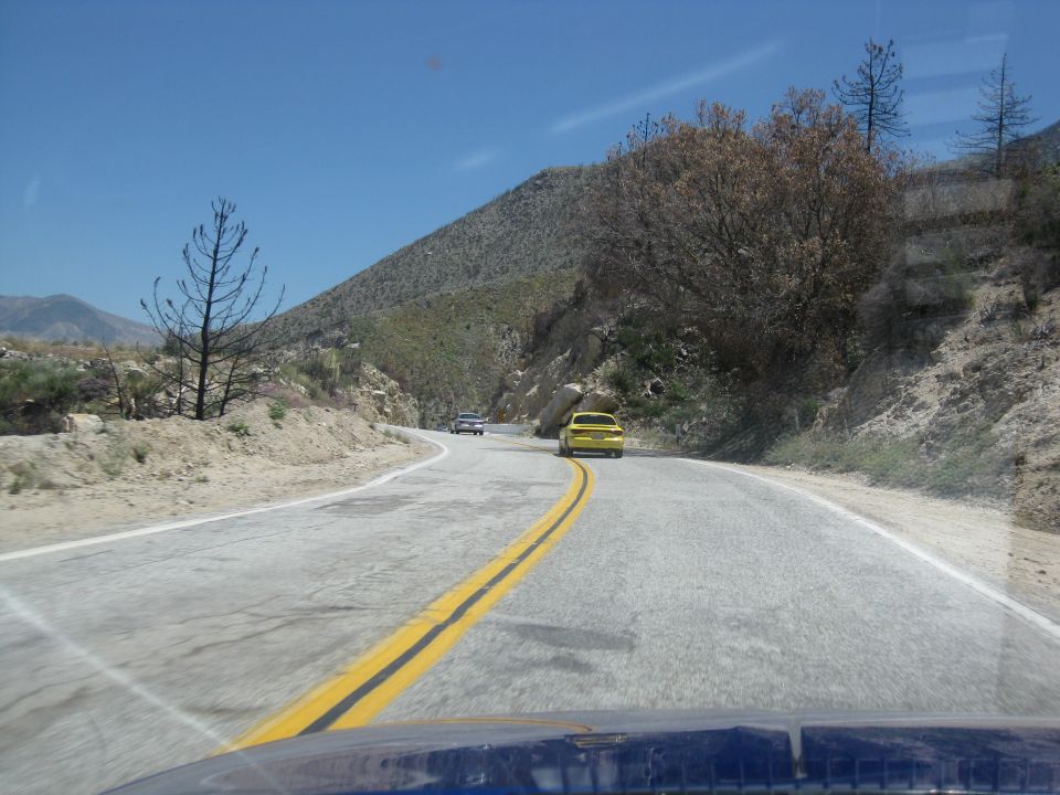 Yellow car and another car drive on a two-lane road through a mountainous, dry landscape