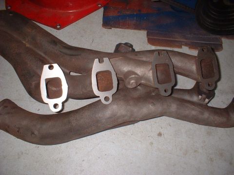 1964 Ford Galaxie - Two exhaust manifolds and three gaskets are laid out on a concrete floor.