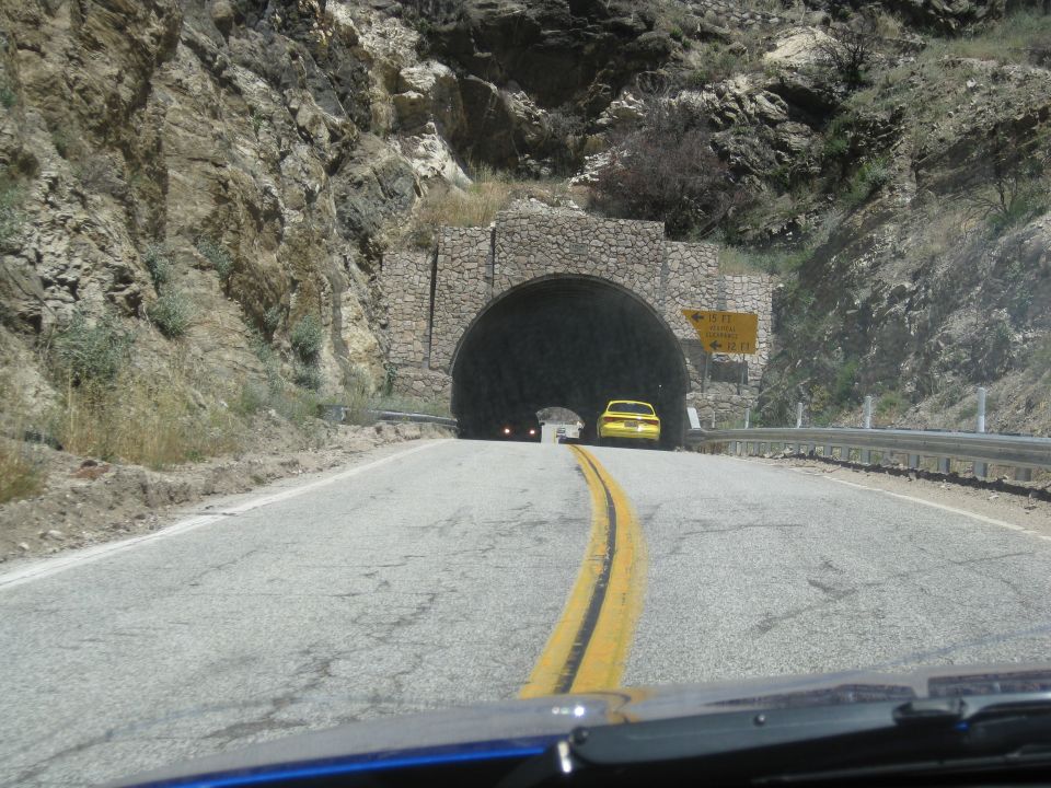 Yellow sedan seen from behind, approaching a stone tunnel entrance on a mountain road