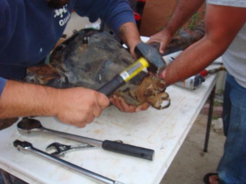 1992 Ford Bronco - Mechanics work on a vehicle's axle assembly, using tools like a hammer and wrenches.