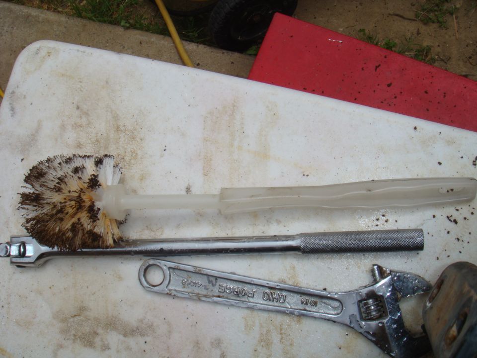 Toilet brush, socket wrench, and adjustable wrench on a white surface