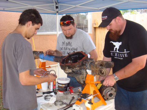1992 Ford Bronco - Three men are gathered around a workbench, focused on assembling a vehicle's axle.