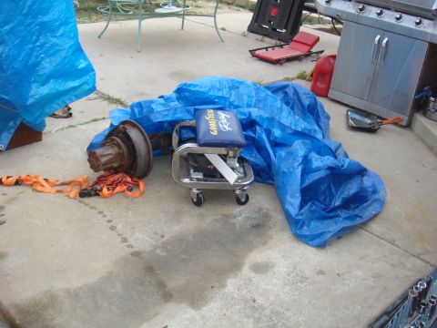 1992 Ford Bronco - An axle assembly lies on the ground next to a blue tarp and a creeper seat.