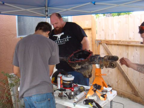 1992 Ford Bronco - People are gathered around a table working on a vehicle's axle assembly, with tools and parts spread out.