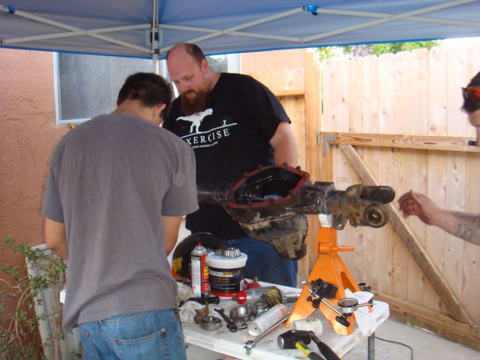 Three people working on a disassembled vehicle axle assembly on a table