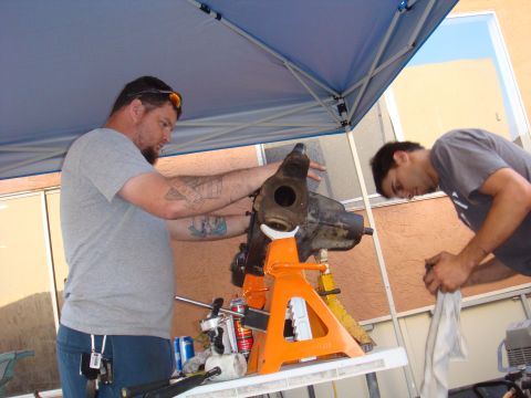 1992 Ford Bronco - Men are working on a vehicle axle assembly outdoors under a blue canopy.