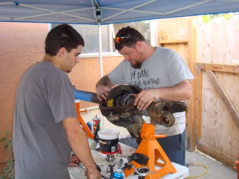 1992 Ford Bronco - Two men work on a vehicle's differential assembly, which is supported by orange jack stands.