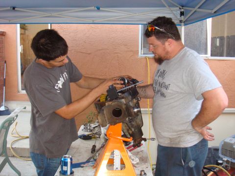 1992 Ford Bronco - Two men are seen working on a vehicle axle assembly that is supported by an orange jack stand.