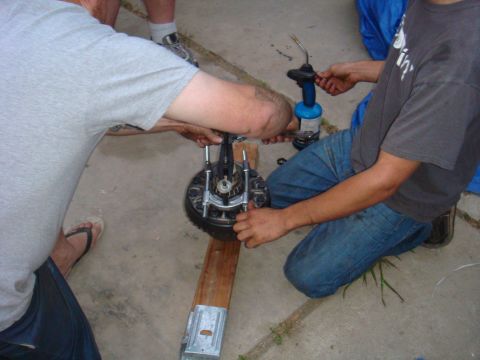 1992 Ford Bronco - Two individuals are seen working on a vehicle's brake assembly, utilizing a torch for what appears to be a repair or modification.