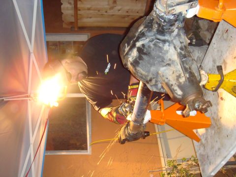 1992 Ford Bronco - A person is welding a vehicle axle that is supported by jack stands.