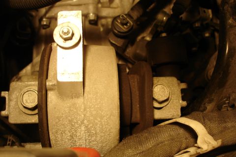 2006 Ford Fusion - Close-up of an engine mount and bracket in an engine bay, showing a metal bracket secured by a large hex bolt to a cylindrical rubber-isola…