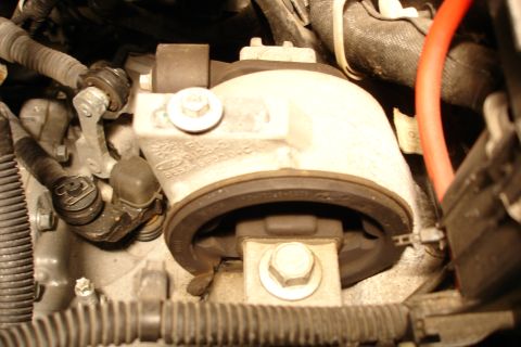 2006 Ford Fusion - Close-up of an aluminum engine mount bracket cast with Ford text ('F6RC' and part markings), secured by a hex bolt at top and another at a…