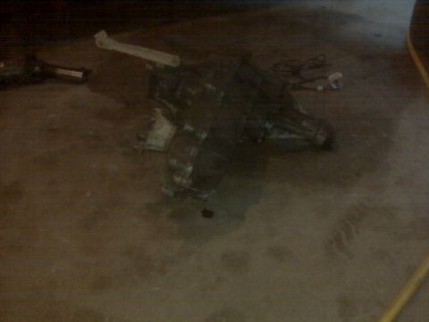 1994 Ford F-250 - A dark transmission part lies on a concrete floor, with some wires visible in the background.