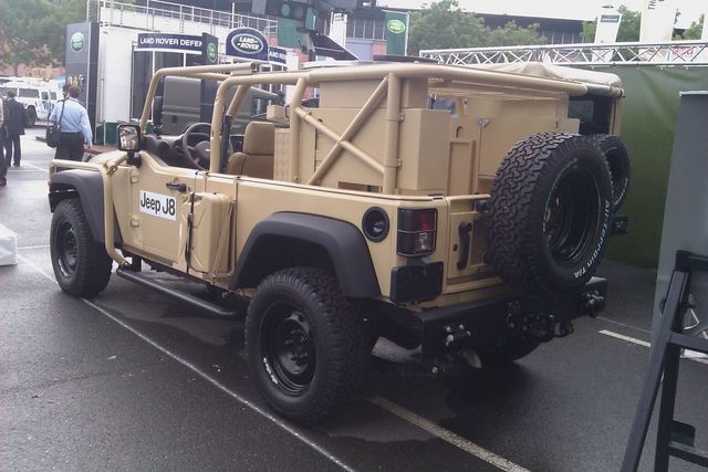 Tan Jeep J8 with roll cage and spare tire mounted on rear