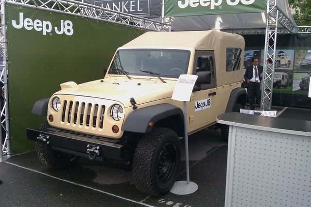 Tan Jeep J8 with a soft top and aftermarket bumper, displayed at an event