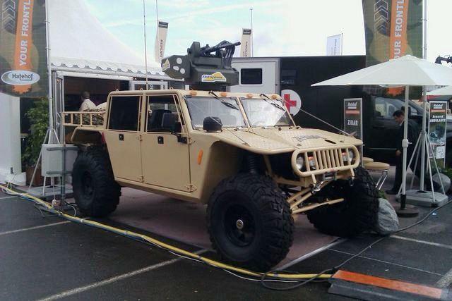 tan 4-door truck with large tires and a weapon system on top, parked near a tent and an ambulance
