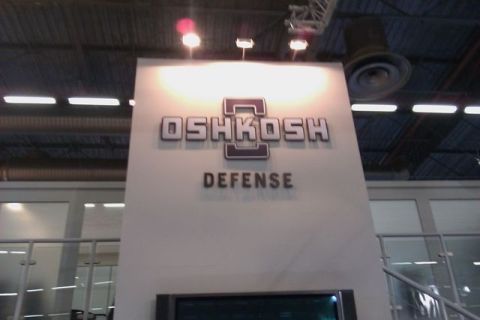 1991 Ford Crown Victoria - Signage for Oshkosh Defense is displayed at an indoor event.