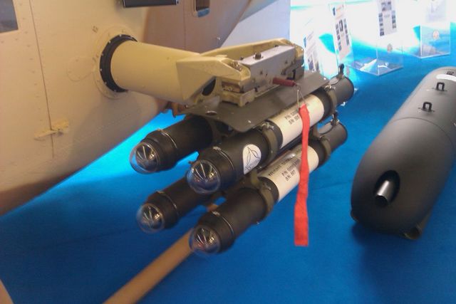 Close-up of a missile pod attached to an aircraft, with a bomb to the right