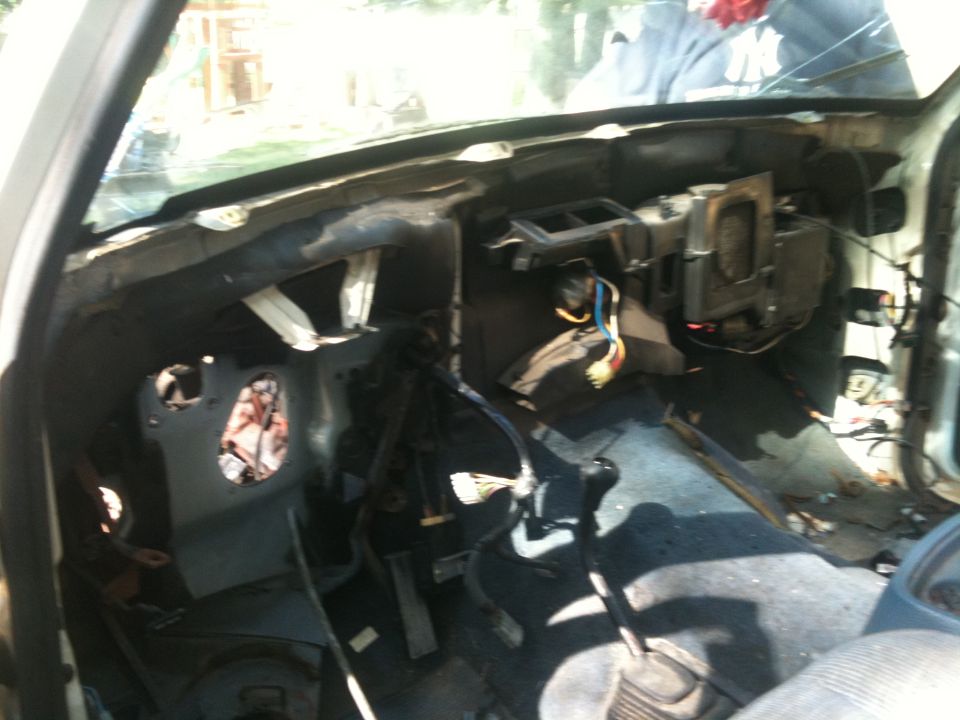 Interior of a dismantled vehicle, showing exposed wires, dashboard components, and pedals