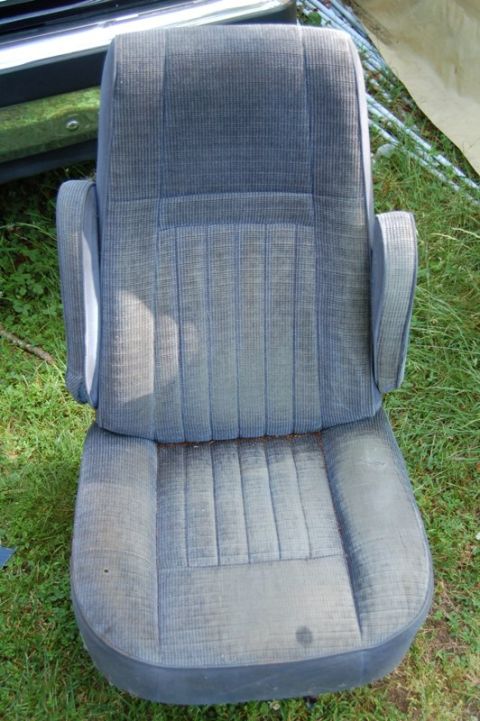 1988 Ford Bronco - A single car seat is shown outdoors, with a portion of a vehicle's front end in the background.