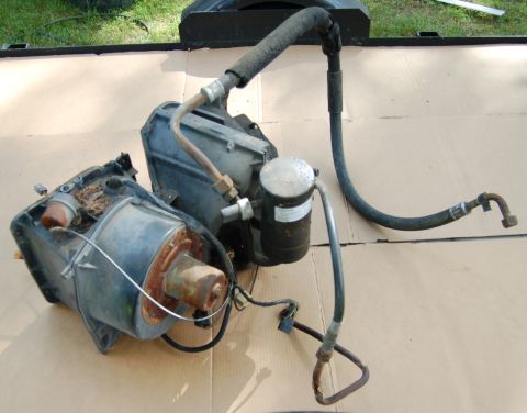 1988 Ford Bronco - Two disassembled automotive air conditioning components, including hoses and a filter, are laid out on a cardboard surface.