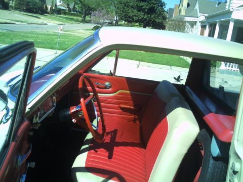 1972 Ford Ranchero - Interior of a vintage car shot down through the open driver's door, showing a red-and-white pleated bench seat, matching red door panel wit…