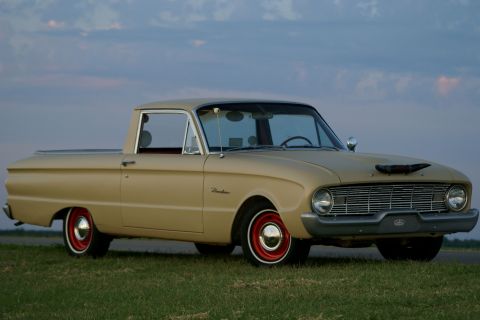 1972 Ford Ranchero - Three-quarter front view of a tan/beige early-1960s Ford Falcon Ranchero car-based pickup parked on grass at dusk, wearing red steel wheels…