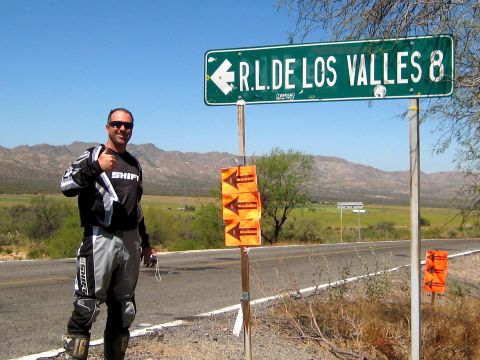 1996 Ford Bronco - Man in motocross gear poses by a road sign in a rural landscape.