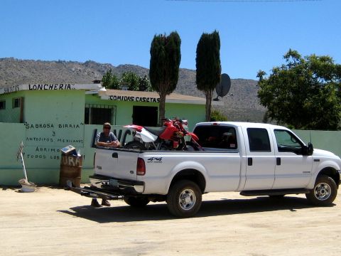 1996 Ford Bronco - A white Ford F-250 pickup truck is parked outside a roadside eatery, with a dirt bike loaded in the bed.