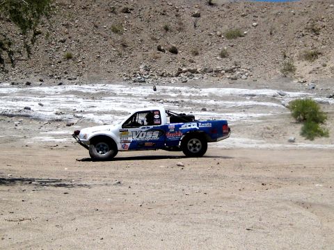 1996 Ford Bronco - A modified pickup truck competes in an off-road race through a dry, rocky terrain.