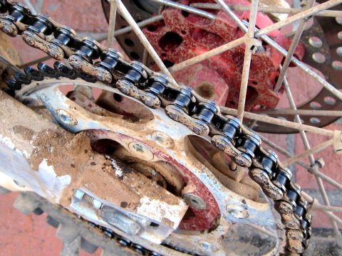 1996 Ford Bronco - Detail of a heavily used motorcycle chain and sprocket, covered in mud and dirt.