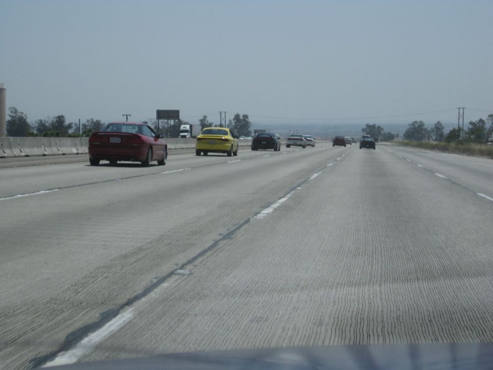 Multiple cars driving on a multi-lane highway under a hazy sky
