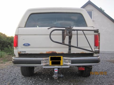 1989 Ford Bronco - Rear view of a white 1989 Ford Bronco, showing its spare tire carrier and some rust on the tailgate.
