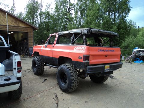 1990 Chevrolet Suburban - Modified orange SUV with a soft top and large off-road tires parked outdoors.