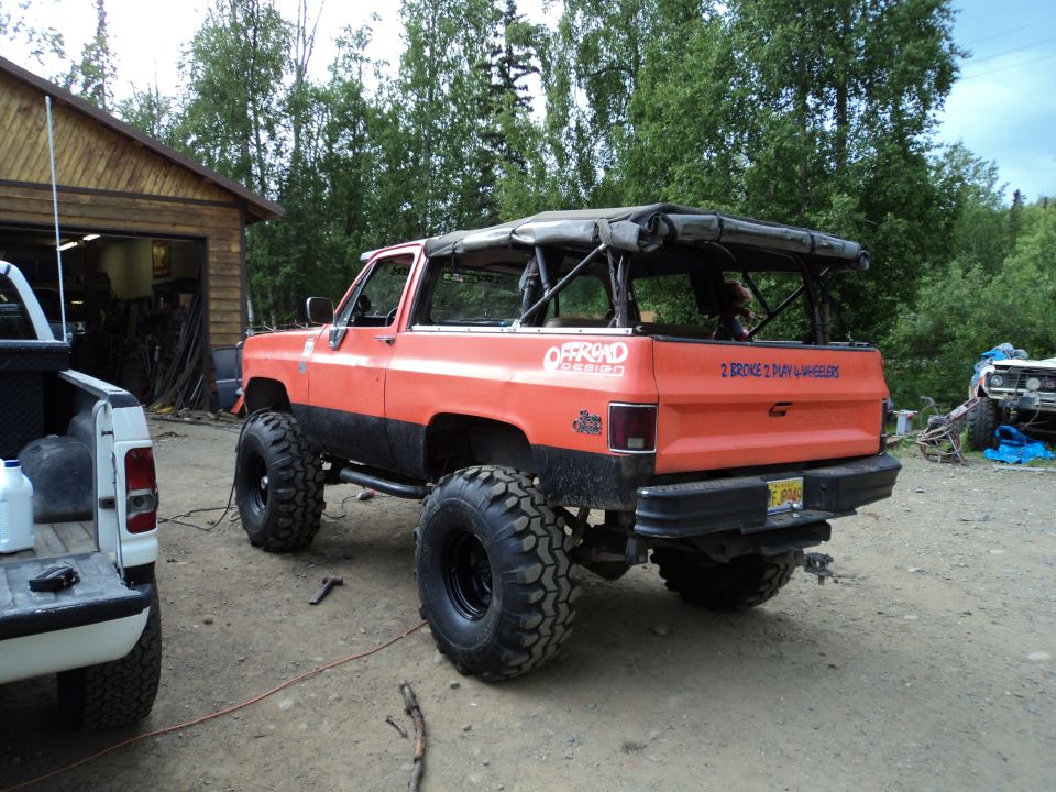 Lifted orange SUV with soft top, off-road tires, and "2 BROKE 2 PLAY & WHEELERS" sticker on tailgate